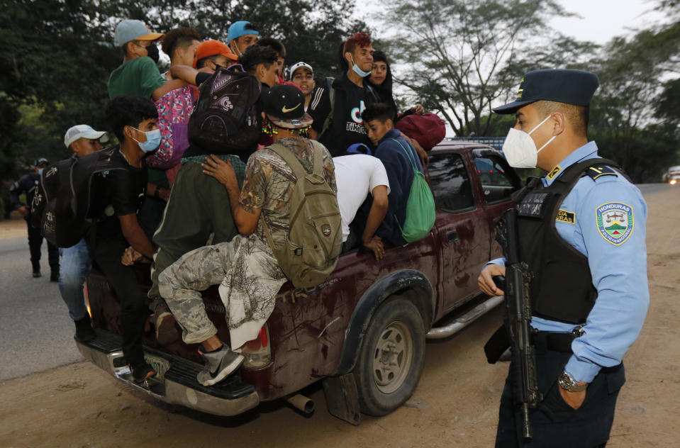A police officer stands by as travelers fill the back of a truck after revising their documents and allowing them to continue their journey toward the Guatemalan border, on the highway leading to Santa Barbara, after they left San Pedro Sula, Honduras, before dawn Friday, Jan. 15, 2021. The migrants left with little certainty about how far they will make it as regional governments appeared more united than ever in stopping their progress. (AP Photo/Delmer Martinez)