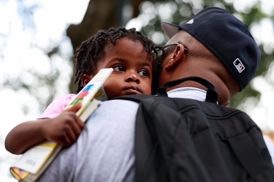 Jamil Davis holds his 3-year-old daughter, Lolonyo, as they listened to speakers Sept. 21, 2023 at James Weldon Johnson Park in Jacksonville, Florida. More than 100 people joined the “Banned Book Readout” hosted by the Association for the Study of African-American Life and History (ASALH). Organizers hosted the readout to protest efforts to ban some books in Florida.