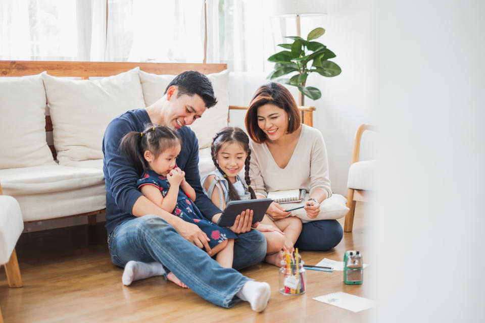 Happy Asian family using tablet, laptop for playing game watching movies, relaxing at home for lifestyle concept