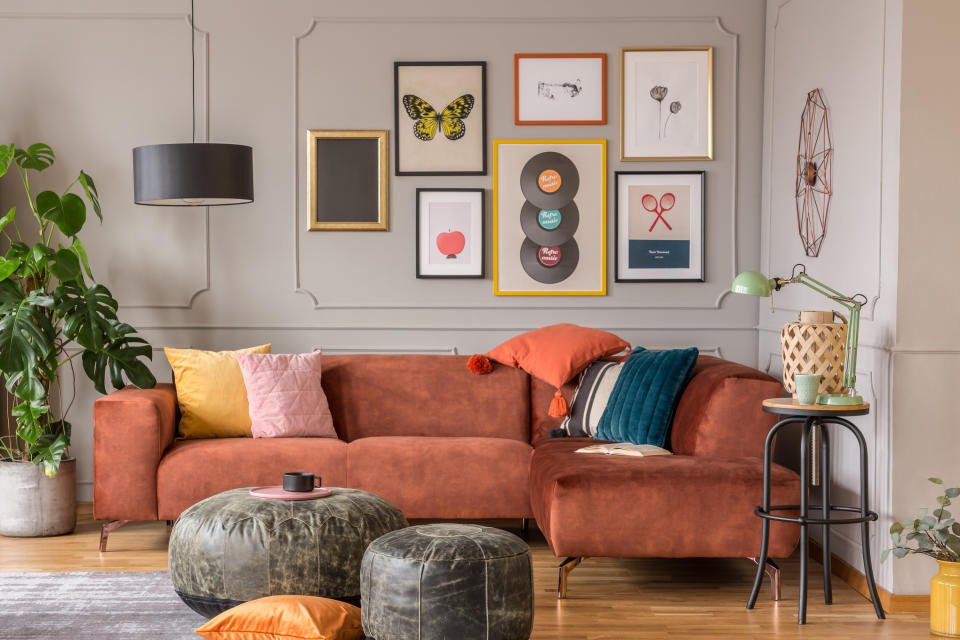 living room with plants, an orange couch, and various colored pillows thrown around (with an eclectic gallery wall behind)