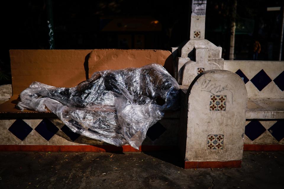 A homeless man cover with a plastic sleeps in a bench of the Condesa neighborhood on April 16 in Mexico City.