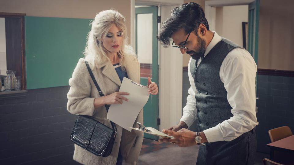 Gemma Arterton in a white coat and holding a script as Barbara and Arsher Ali in a dark waistcoat and glasses as Dennis in Funny Woman