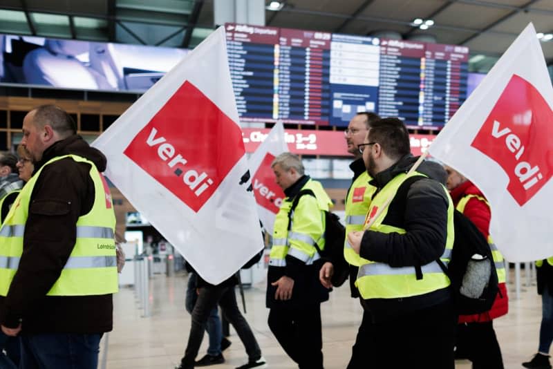 Aviation security staff demonstrate with flags from the service union Verdi in the departure hall in Terminal 1 at BER Airport. After several rounds of strikes at Germany's airports, arbitration for private aviation security staff began on Friday at a secret location. Carsten Koall/dpa