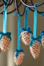 <p>Hang these lighter, brighter fall standbys from your chandelier with colorful velvet ribbon.</p><p><strong>Step 1: </strong>Mix two parts bleach with one part water in a bucket. Submerge pinecones in sol-ution for 24 hours. (Tip: Place a plate or another heavy object on top to keep them under water.) Rinse them in water and set outside to dry until they open up again. (This could take up to a week, depending on the weather.) </p><p><strong><strong>Step 2: </strong> </strong>Cut 1 yard of velvet ribbon into a ¾-yard piece and a ¼-yard piece.</p><p><strong>Step 3: </strong>Adhere end of longer ribbon to the pinecone base with hot glue. Tie the shorter ribbon into a bow; adhere to the base of the pinecone, as shown.</p><p><strong>Step 4: </strong> Tie pinecones to chandelier arms. Trim excess ribbon. </p>