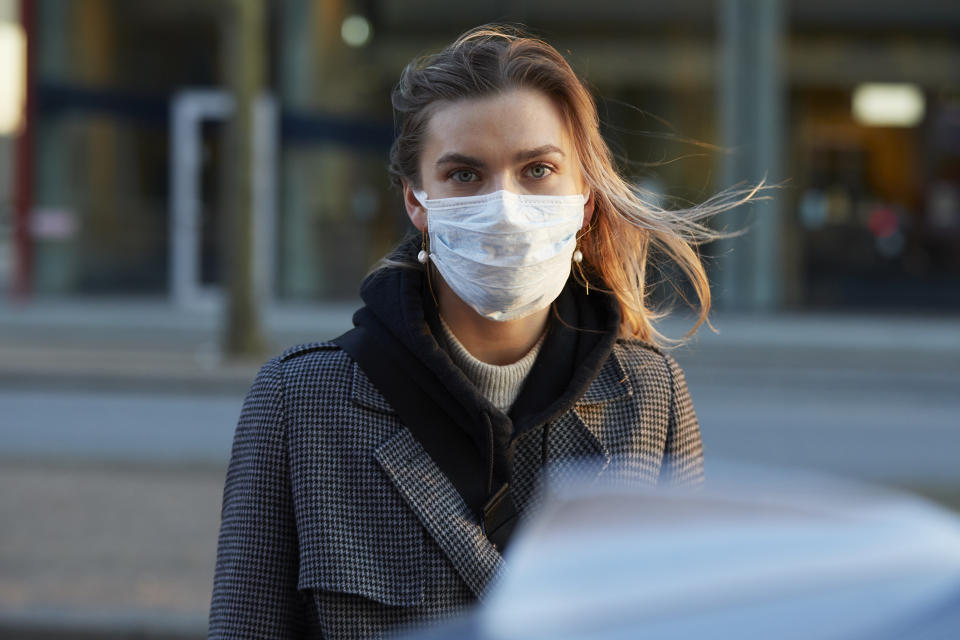 Young woman standing on city street wearing protective face mask