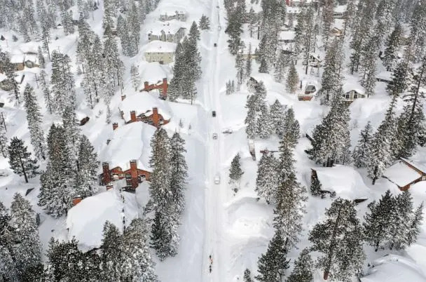 PHOTO: Snowboarders walk and cars attempt to drive in the Sierra Nevada mountains, as now reached record levels, March 29, 2023 in Mammoth Lakes, Calif. (Mario Tama/Getty Images)