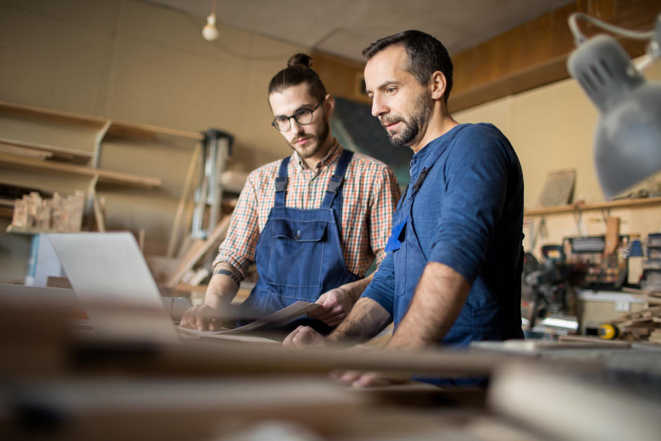 Low angle portrait of two modern artisans using laptop in workshop while working with wood together, copy space