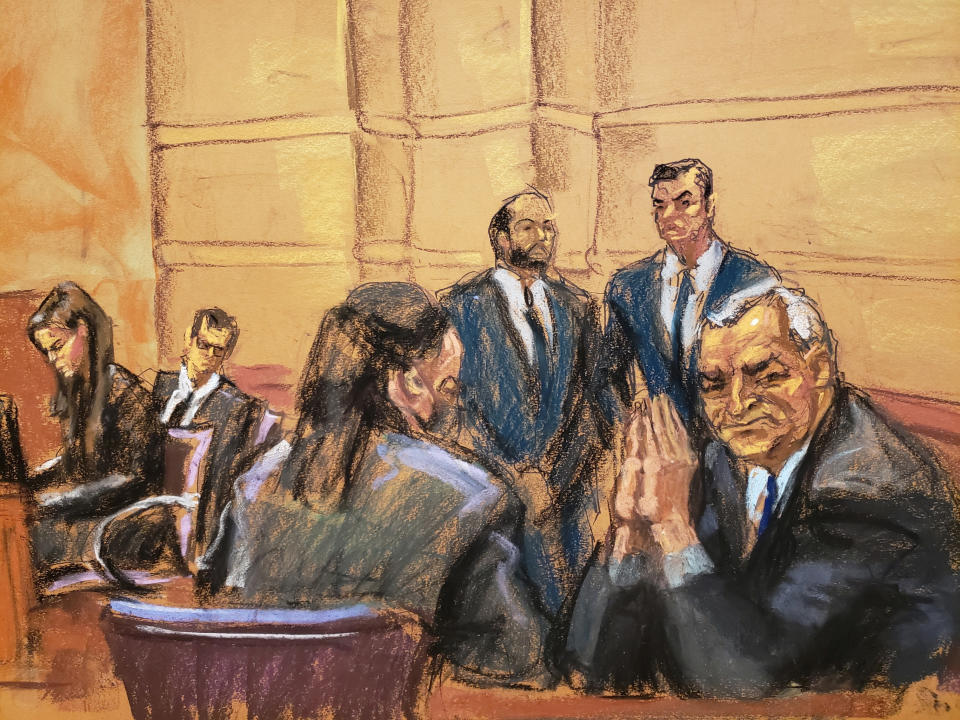 Courtroom sketch of Garcia Luna seated at a table near others with his elbows resting on the table and his palm pressed together by his face.