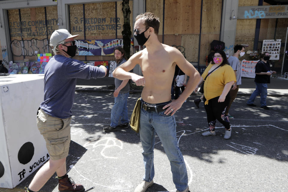 Protesters bump elbows in greeting as they work on barricades in the street adjacent to a closed police precinct Thursday, June 18, 2020, in Seattle, in what has been named the Capitol Hill Occupied Protest zone. Police pulled back from several blocks of the city's Capitol Hill neighborhood near the Police Department's East Precinct building earlier in the month after clashes with people protesting the death of George Floyd in Minneapolis. (AP Photo/Elaine Thompson)