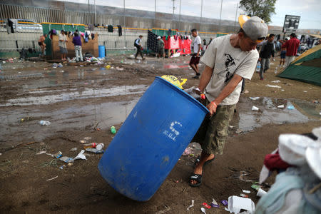 A migrant, part of a caravan of thousands from Central America trying to reach the United States, drags a trash can past showers in a temporary shelter in Tijuana, Mexico, November 28, 2018. REUTERS/Lucy Nicholson