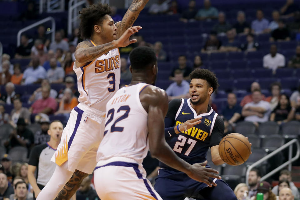 Denver Nuggets guard Jamal Murray (27) dishes around Phoenix Suns forward Kelly Oubre Jr. (3) and center Deandre Ayton (22) during the first half of an NBA preseason basketball game, Monday, Oct. 14, 2019, in Phoenix. (AP Photo/Matt York)