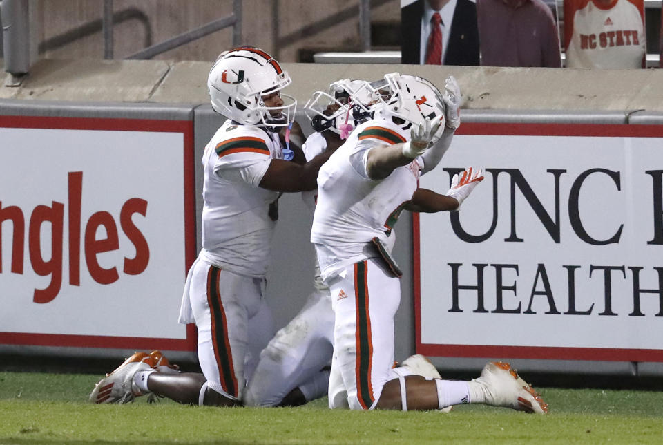 Miami's Mark Pope, left and Jaylan Knighton, right, celebrate with Mike Harley, rear, after Harley scored on 54-yard touchdown during the second half of Miami's 44-41 victory over North Carolina State in an NCAA college football game Friday, Nov. 6, 2020, in Raleigh, N.C. (Ethan Hyman/The News & Observer via AP, Pool)