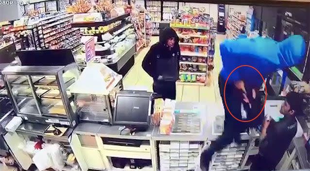 Two hooded thieves enter the store and jump over the front counter, threatening the attendant.