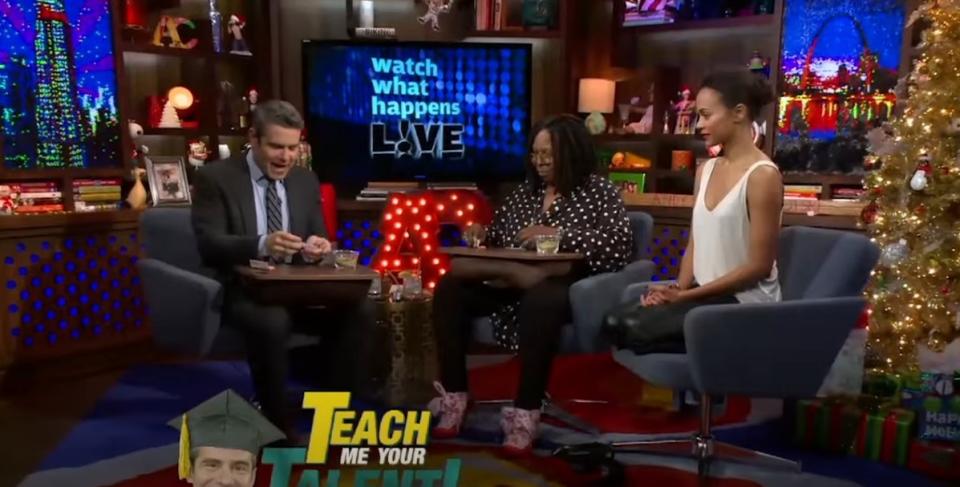 Andy Cohen learning how to roll a joint from Whoopi Goldberg while Zoe Saldana watches