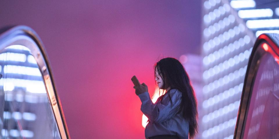 A stock image of a woman in on her phone in Shanghai, against a pink and purple sky