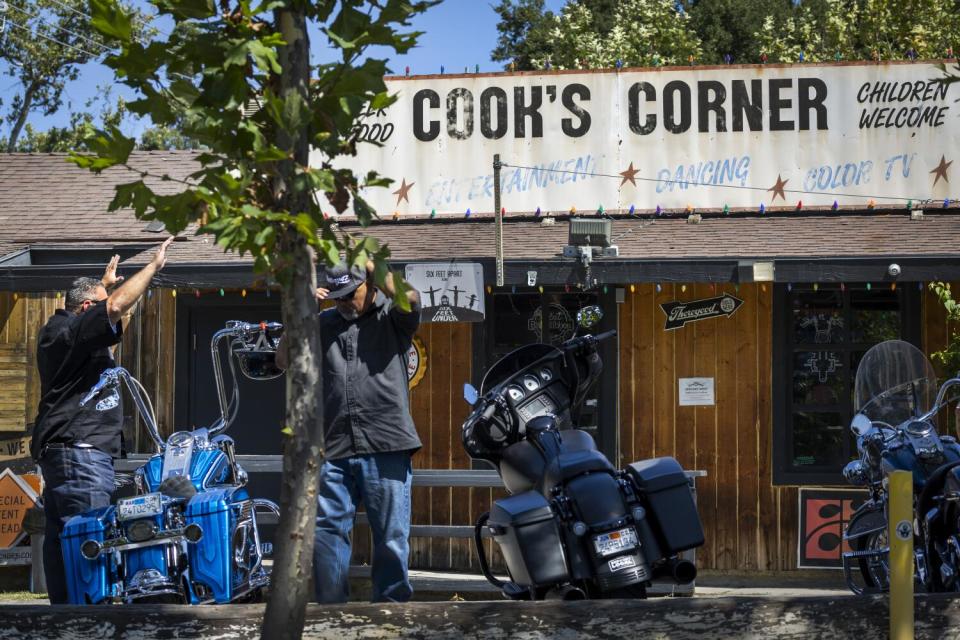 One man lifts his arms in prayer as he and friend stand next to their motorcycles.