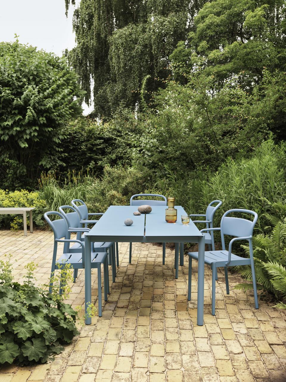 A backyard with brick flooring and a blue steel table and chairs