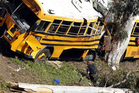 A police officer inspects a school bus leaning against a tree after it veered off the road in Anaheim, southern California April 24, 2014. REUTERS/Alex Gallardo