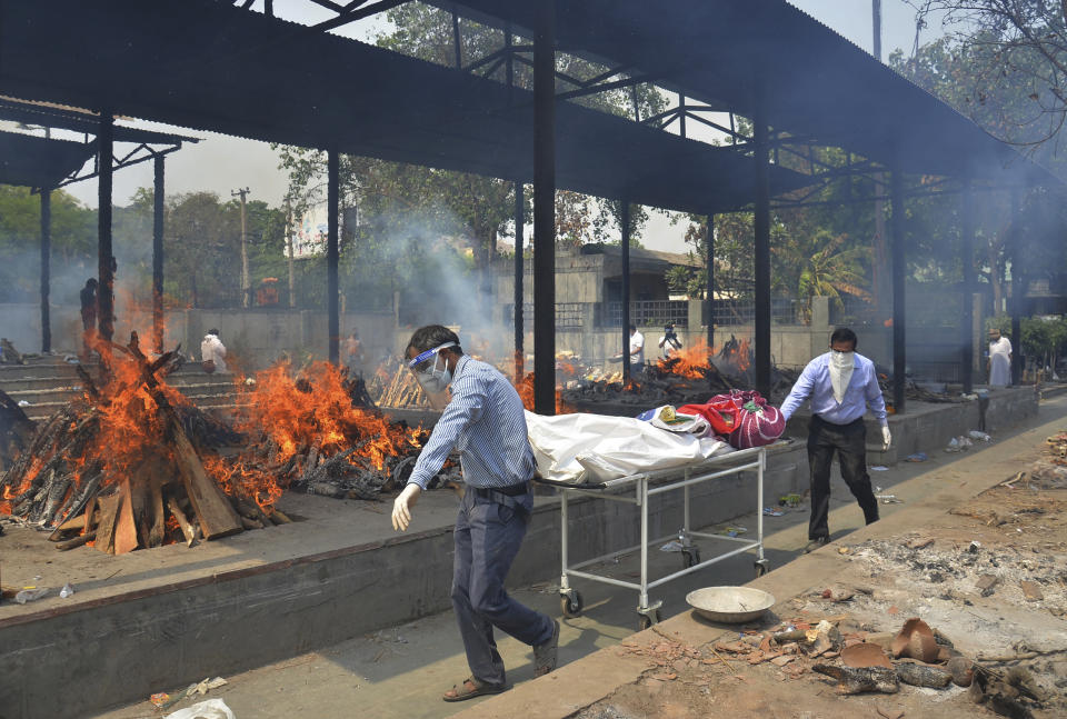 FILE - In this May 1, 2021, file photo, relatives carry the body of a person who died of COVID-19 as multiple pyres of other COVID-19 victims burn at a crematorium in New Delhi, India. COVID-19 infections and deaths are mounting with alarming speed in India with no end in sight to the crisis. People are dying because of shortages of bottled oxygen and hospital beds or because they couldn’t get a COVID-19 test. (AP Photo/Amit Sharma, File)