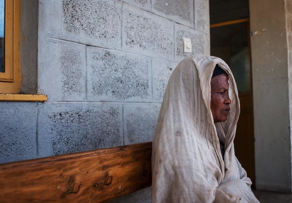 Bugune, wrapped in a shawl on a bench outside her local health clinic, is recovering from eyelid surgery that saved her sight. (Photo: Tom Gardner)