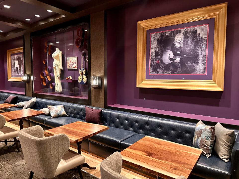 Purple room with purple couches and beige chairs with framed photos of Dolly Parton and outfits/guitars of her on display in glass boxes on the wall