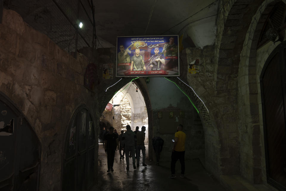 Palestinians walk under a banner depicting militants from the Lions' Den group who were killed by Israeli forces, from left, Fadi Qufesheh, Abdulrahman Soboh, Mohammad Azizi and Mahmoud Zakari, in al-Yasmeena quarter of the Old City of Nablus, in the West Bank, Thursday, May 4, 2023. The killing of Zuhair al-Ghaleeth last month, the first slaying of a suspected Israeli intelligence collaborator in the West Bank in nearly two decades, has laid bare the weakness of the Palestinian Authority and the strains that a recent surge in violence with Israel is beginning to exert within Palestinian communities. (AP Photo/Nasser Nasser)