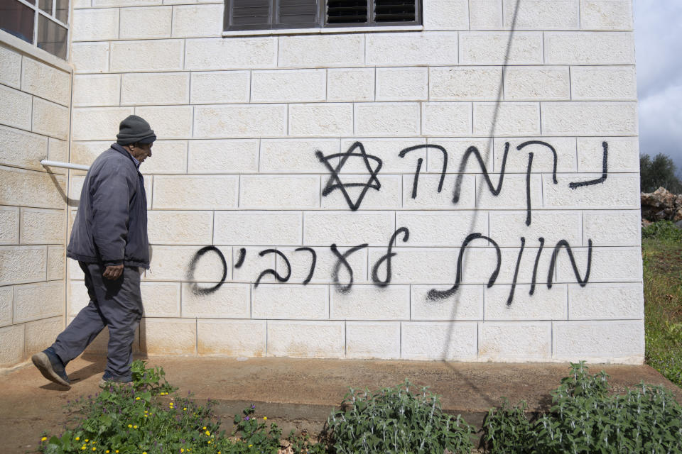 A man looks at graffiti that reads, in Hebrew, "revenge, death to Arabs," allegedly sprayed by Jewish West Bank settlers in the Palestinian West Bank village of Turmus Ayya, Sunday, Feb. 18, 2024. Village residents claimed that settlers raided the outskirts of the village overnight, setting fire to a car and spaying graffiti on the walls of homes. (AP Photo/Nasser Nasser)