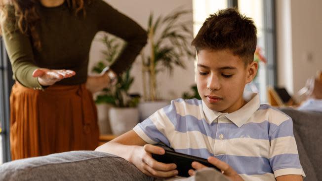 Adolescente con su celular y madre detrás.