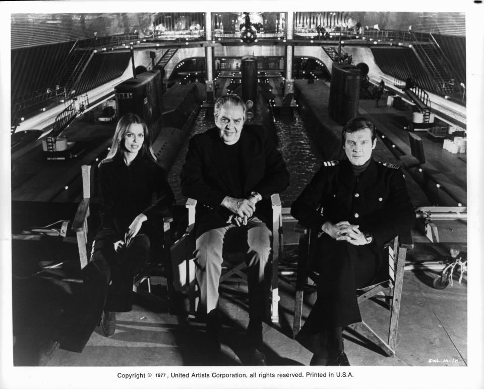 Actors Barbara Bach and Roger Moore sitting in front of a submarine tank at Pinewood Studios with producer Albert R. Broccoli between them, during the making of the James Bond film 'The Spy Who Loved Me', 1977. (Photo by United Artist/Getty Images)