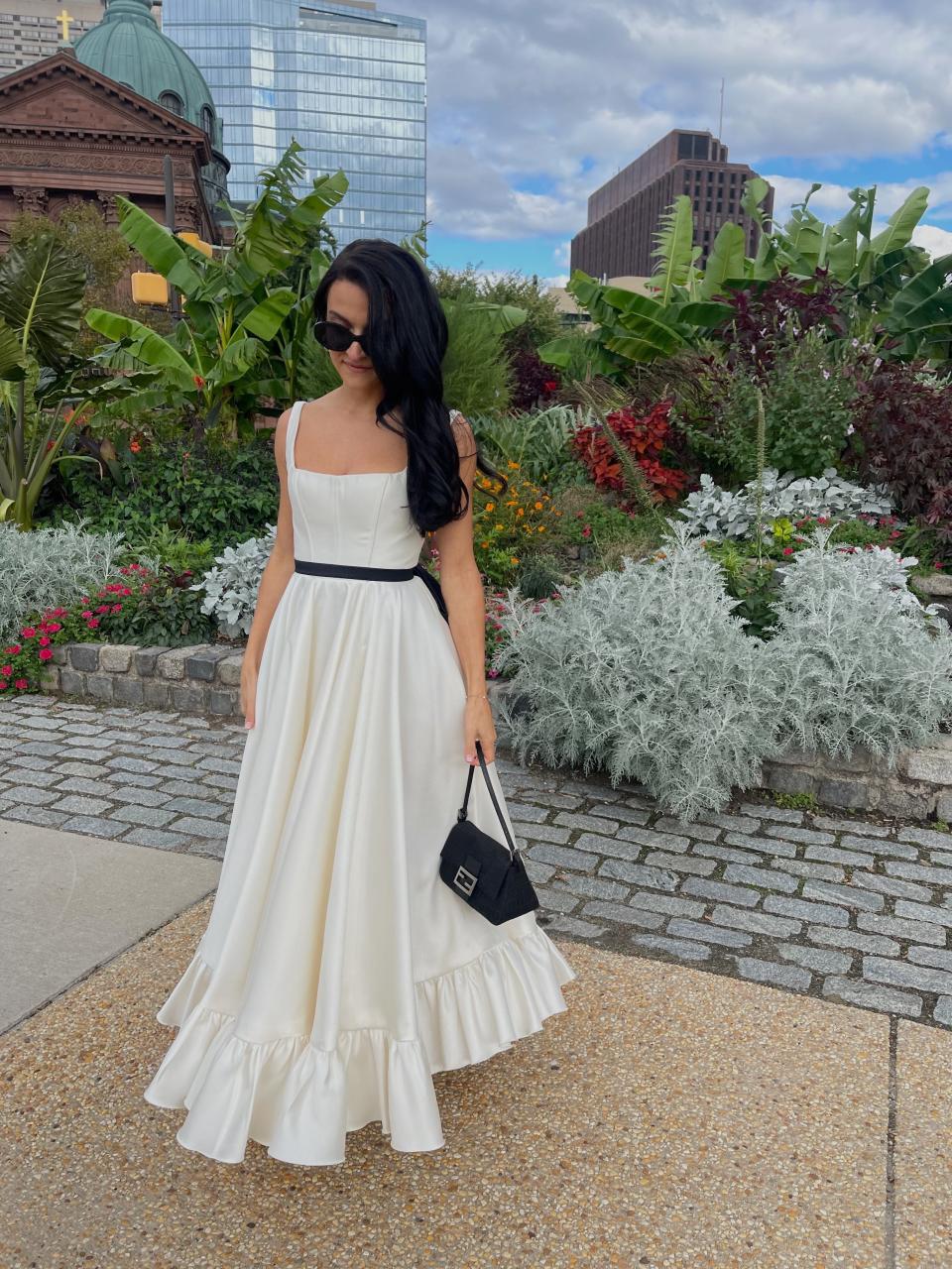 A woman stands in a white dress with a black belt.