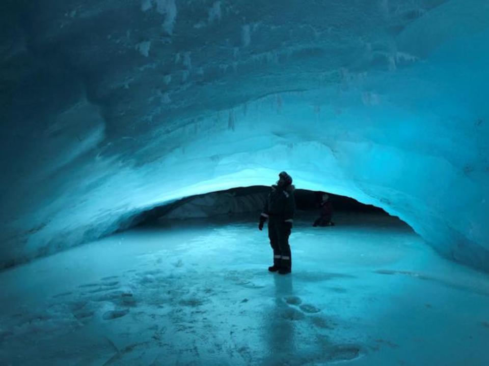 A researcher is in a cave formed under the ice in the Arctic Svalbard glaciers. The person's shape is cast against the eery blue light filtering through the thin ice.