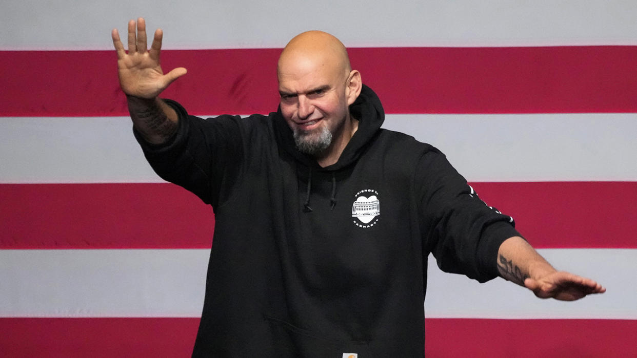 Lt. Gov. John Fetterman waves to his supporters, against a wall of red and white stripes.