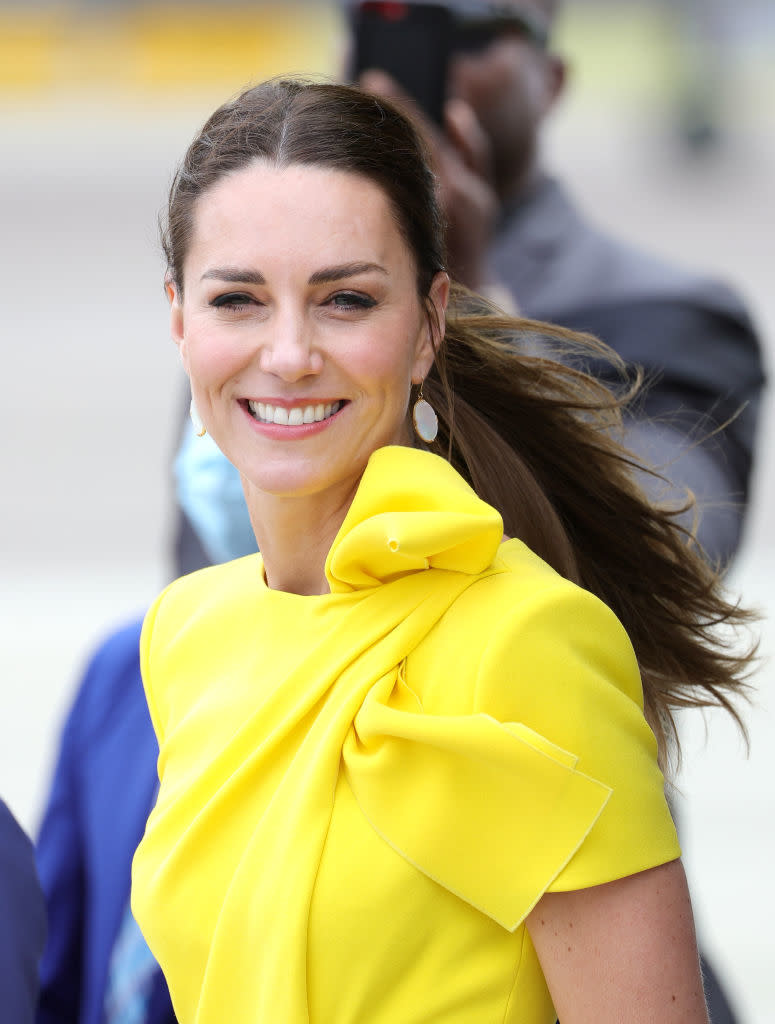 Kate Middleton smiling, wearing a dress with a bow detail at the neck