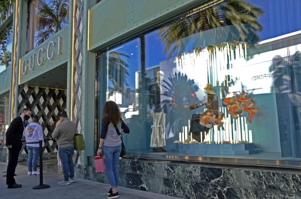 An employee at Gucci talks to a man waiting on a socially distanced line of shoppers waiting to enter the luxury designer boutique on Rodeo Drive, Thursday, Dec. 3, 2020, in Beverly Hills, Calif. The new stay-at-home order will last at least three weeks, cutting sharply into the most profitable shopping season and threatening financial ruin for businesses already struggling after 10 months of on-again, off-again restrictions and slow sales because of the pandemic. (AP Photo/Pamela Hassell)