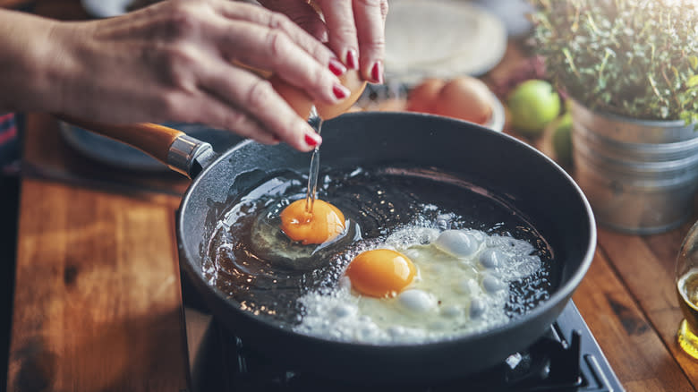 Hands cracking eggs into pan 