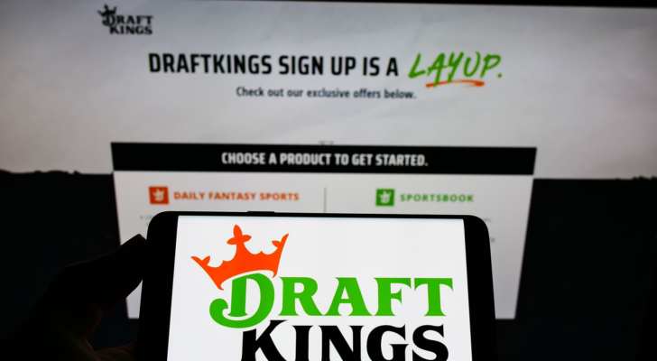 Person holding smartphone with logo of US sports betting company DraftKings Inc. (DKNG) on screen in front of website. Focus on phone display. Unmodified photo.