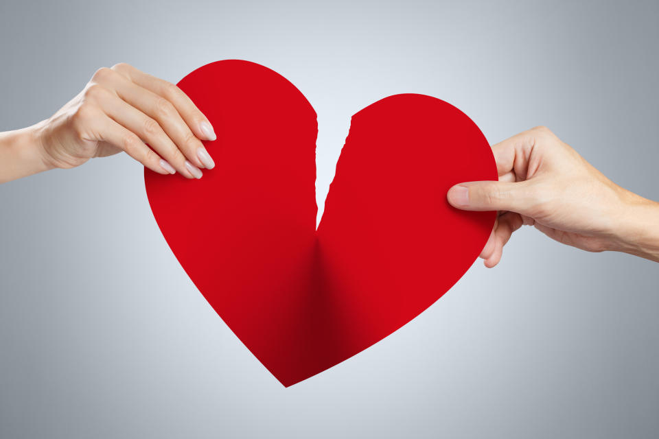 Two hands, one female and one male, holding the torn pieces of a red heart