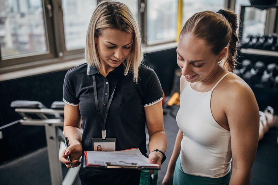 A female personal trainer holding a clipboard and talking to a female client