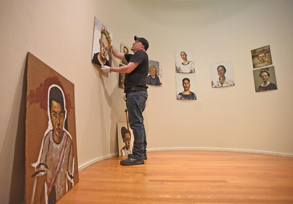 Jerry Francl carefully places John Mellencamp's art on the wall of the Mansfield Art Center.