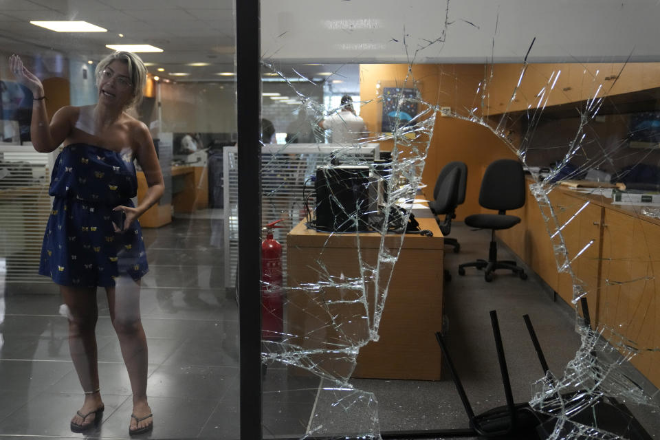 A bank employee gestures, as she stands next to a window broken by depositors to exit the bank, in Beirut, Lebanon, Wednesday, Sept. 14, 2022. An armed woman and a dozen activists broke into a Beirut bank branch on Wednesday, taking over $13,000 from what she says were from her trapped savings. Lebanon's cash-strapped banks since 2019 have imposed strict limits on withdrawals of foreign currency, tying up the savings of millions of people. (AP Photo/Hussein Malla)