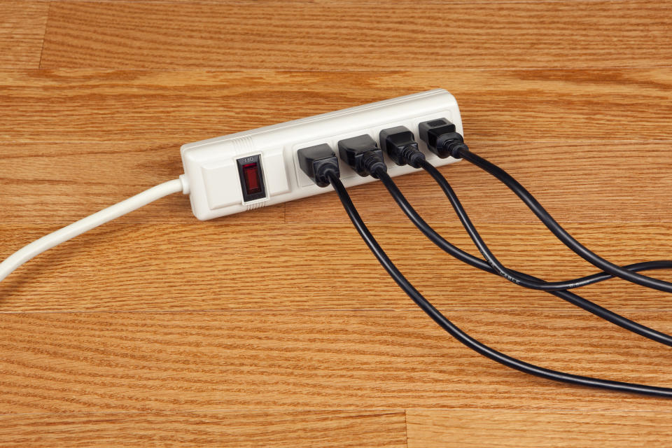Power strip with multiple plugs inserted, switch is in off position, on a wooden surface