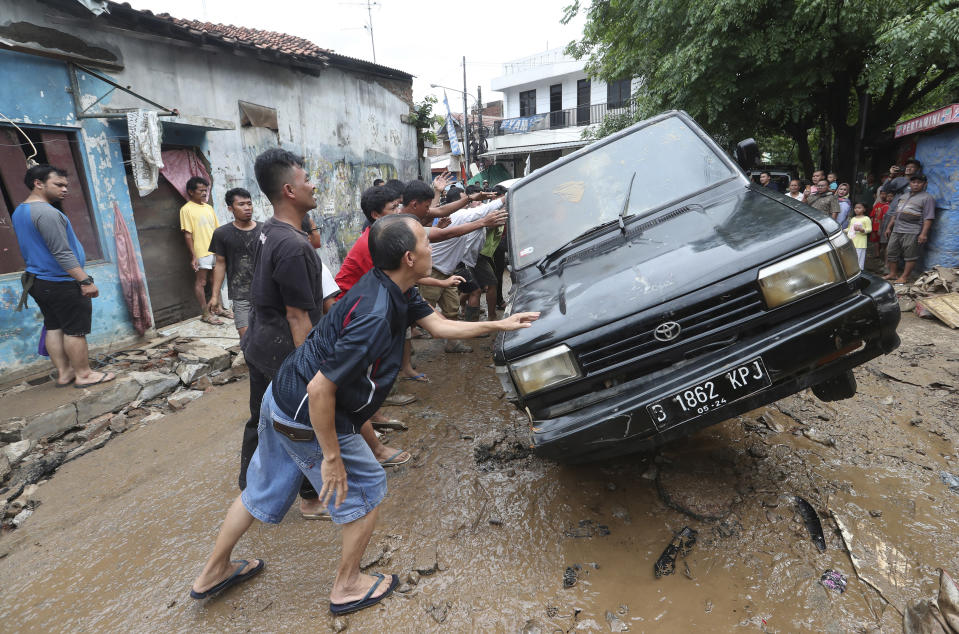 Residents move the wreckage of cars that were swept away by flood in Bekasi, West Java, Indonesia, Friday, Jan. 3, 2020.Severe flooding in greater Jakarta has killed scores of people and displaced tens of thousands others, the country's disaster management agency said. (AP Photo/Achmad Ibrahim)