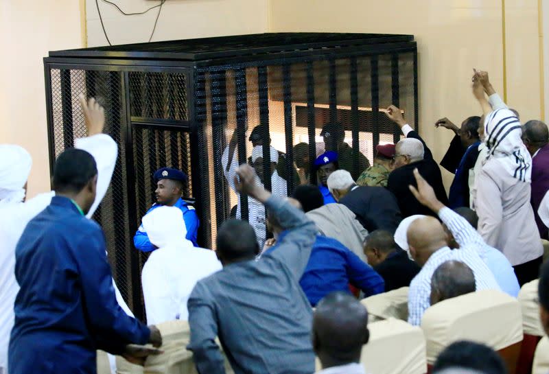 Sudanese former president Omar Hassan al-Bashir waves to supporters as he sits inside a cage during the hearing of the verdict that convicted him of corruption charges in a court in Khartoum