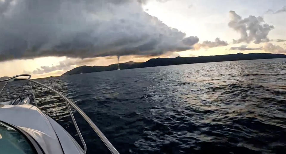 Two waterspouts can be seen in the distance as a boat cruises through the water towards Hayman Island.