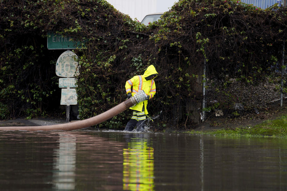 A worker carries a hose on a flooded street Thursday, Feb. 1, 2024 in Long Beach, Calif. (AP Photo/Eric Thayer)