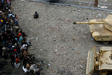 FILE PHOTO: An anti-government protester prays as his comrades stand behind barbed wire in front of army tanks alongside the Egyptian Museum on the front line near Tahrir Square in Cairo, Egypt, February 5, 2011. REUTERS/Yannis Behrakis/File photo
