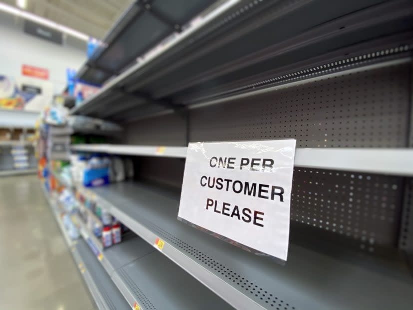 Ein Zettel mit der Aufschrift: „One per Customer“, der an einem leeren Supermarktregal hängt.