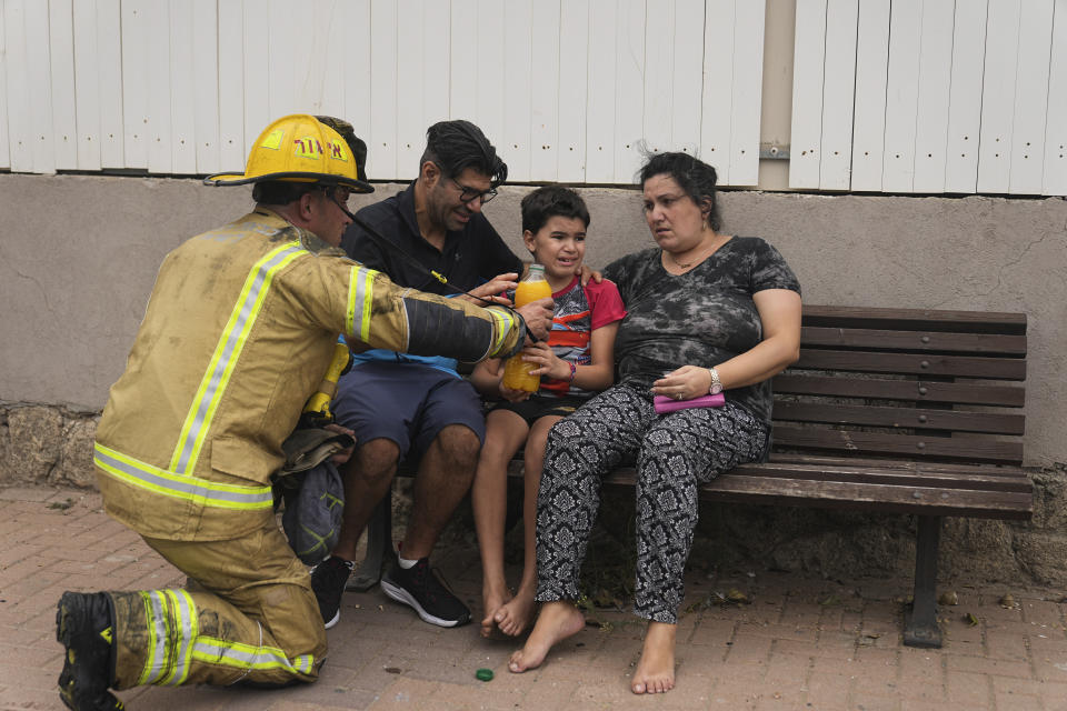 An Israeli firefighter hands a drink to a young child next to a site struck by a rocket fired from the Gaza Strip, in Ashkelon, southern Israel, Monday, Oct. 9, 2023. (AP Photo/Ohad Zwigenberg)