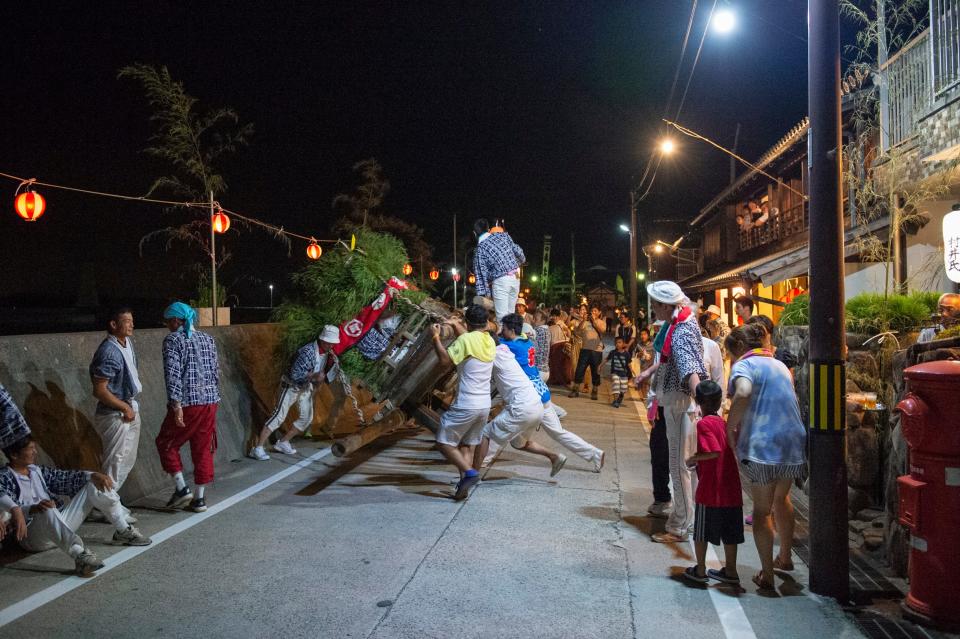 Men on the street in Japan at night carrying a wooden structure for a festival