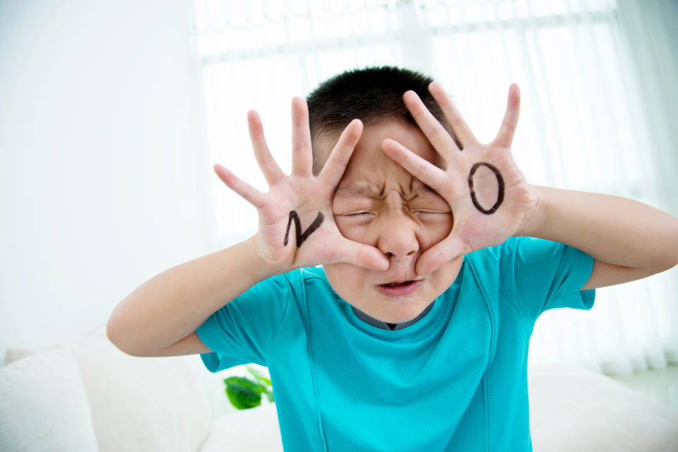 Child in a blue shirt holding their hands in front of their face with 